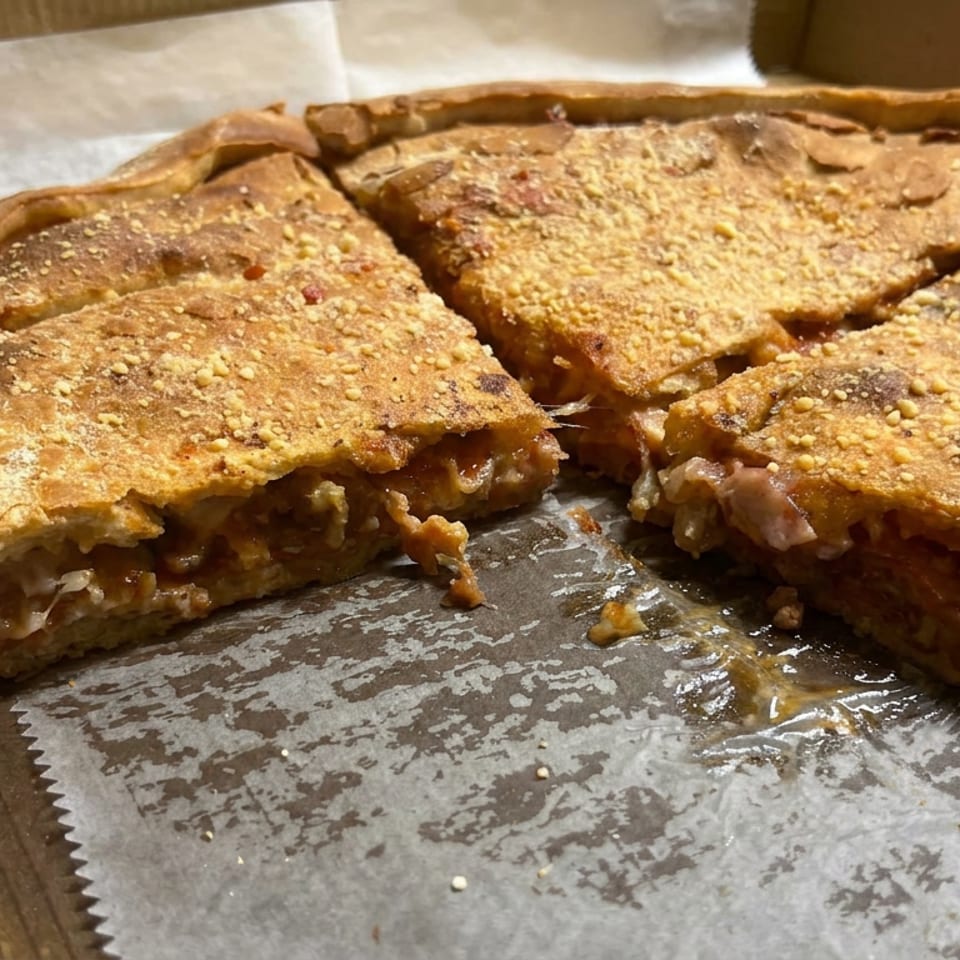 Four cheesy, sauce-filled pizza slices with sesame seeds sit in a cardboard takeaway box.